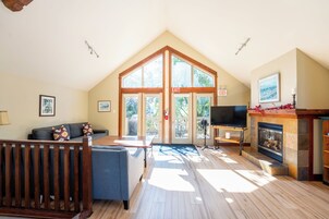 A spacious living room with a high ceiling, a fireplace, a television, and a large sliding glass door leading to an outdoor area.