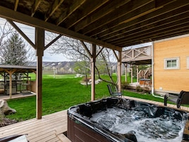 Un jacuzzi debajo de una terraza de madera, con vista a un césped y una casa al fondo.
