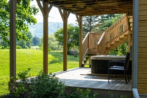 Una terraza de madera con un jacuzzi y sillas, con vistas a un paisaje cubierto de hierba y colinas.