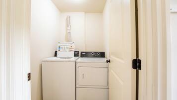A compact laundry room with a washing machine and dryer, a control panel, and a ventilation duct.