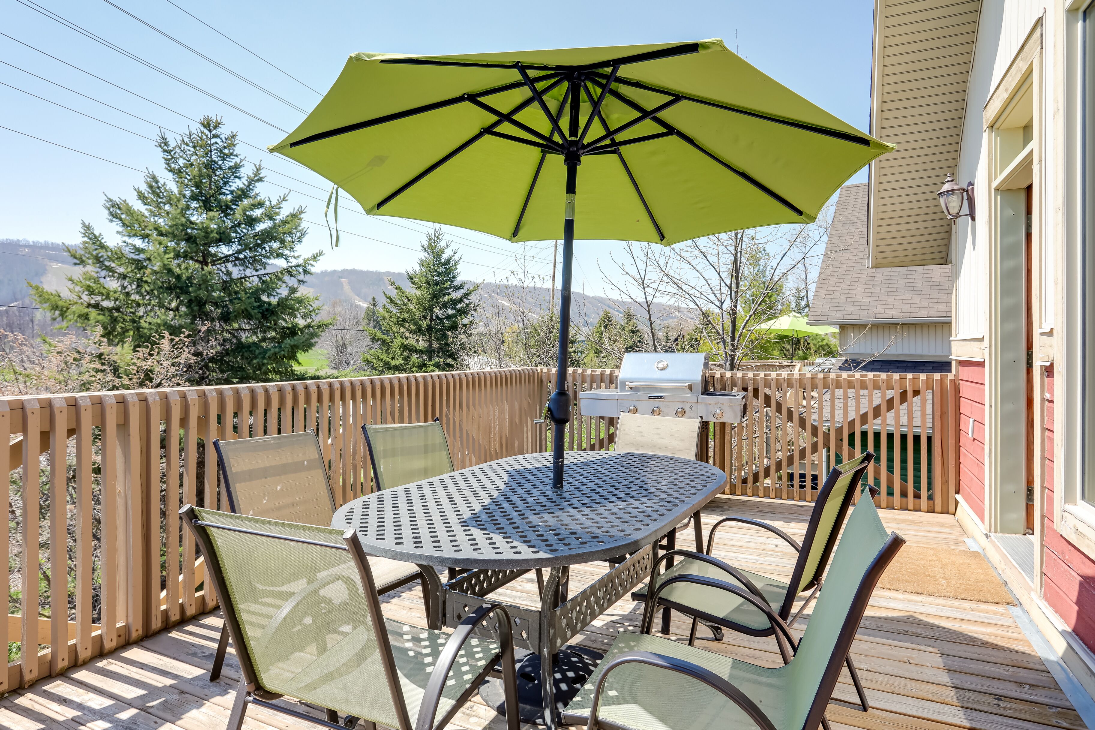 En terrasse med et rundt metalbord og stole, en gul parasol og en grill.