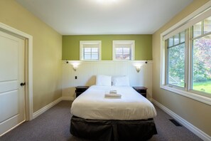 Un dormitorio con una cama, dos mesitas de noche, una ventana y una puerta.