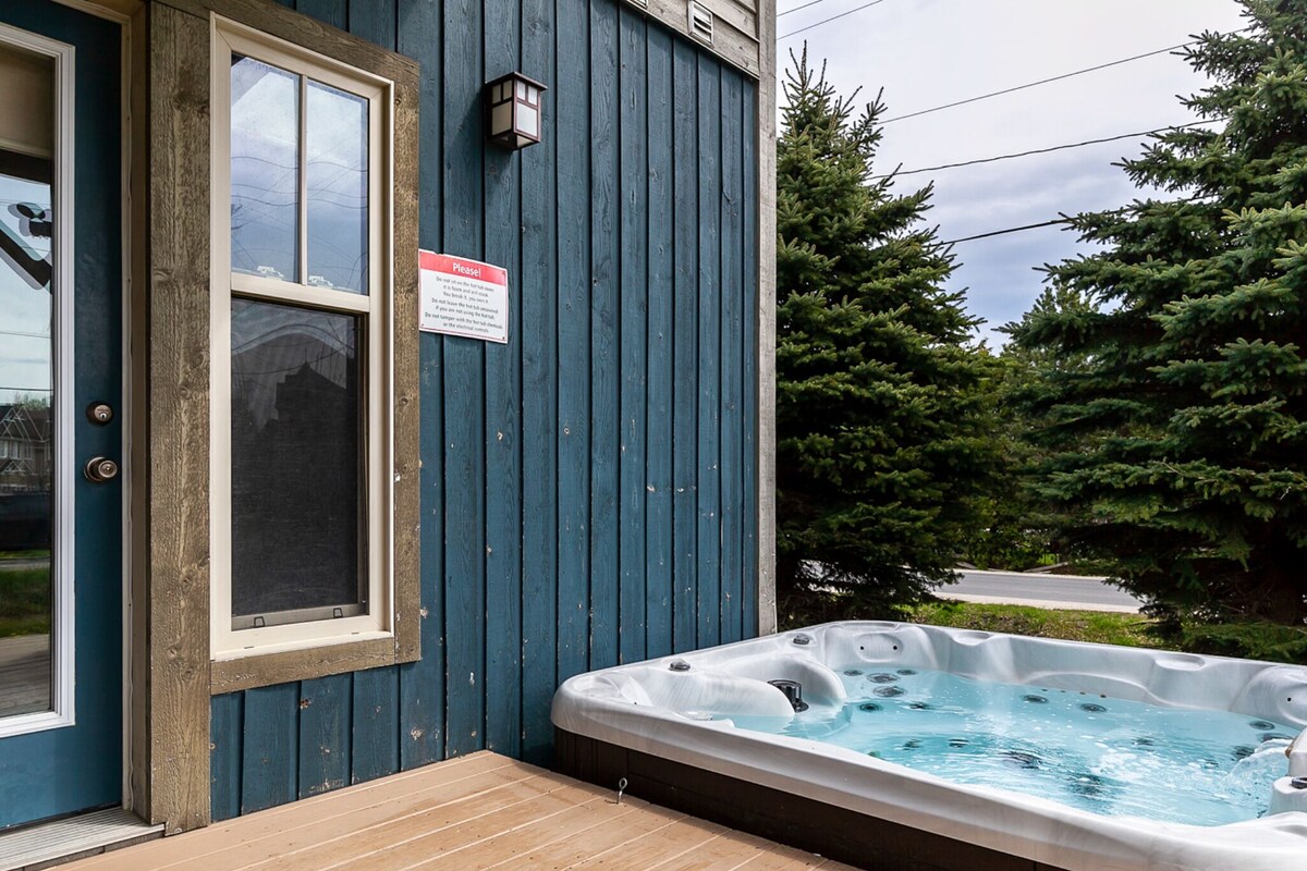 Une terrasse en bois avec un jacuzzi, une porte avec une fenêtre et un panneau sur le mur.