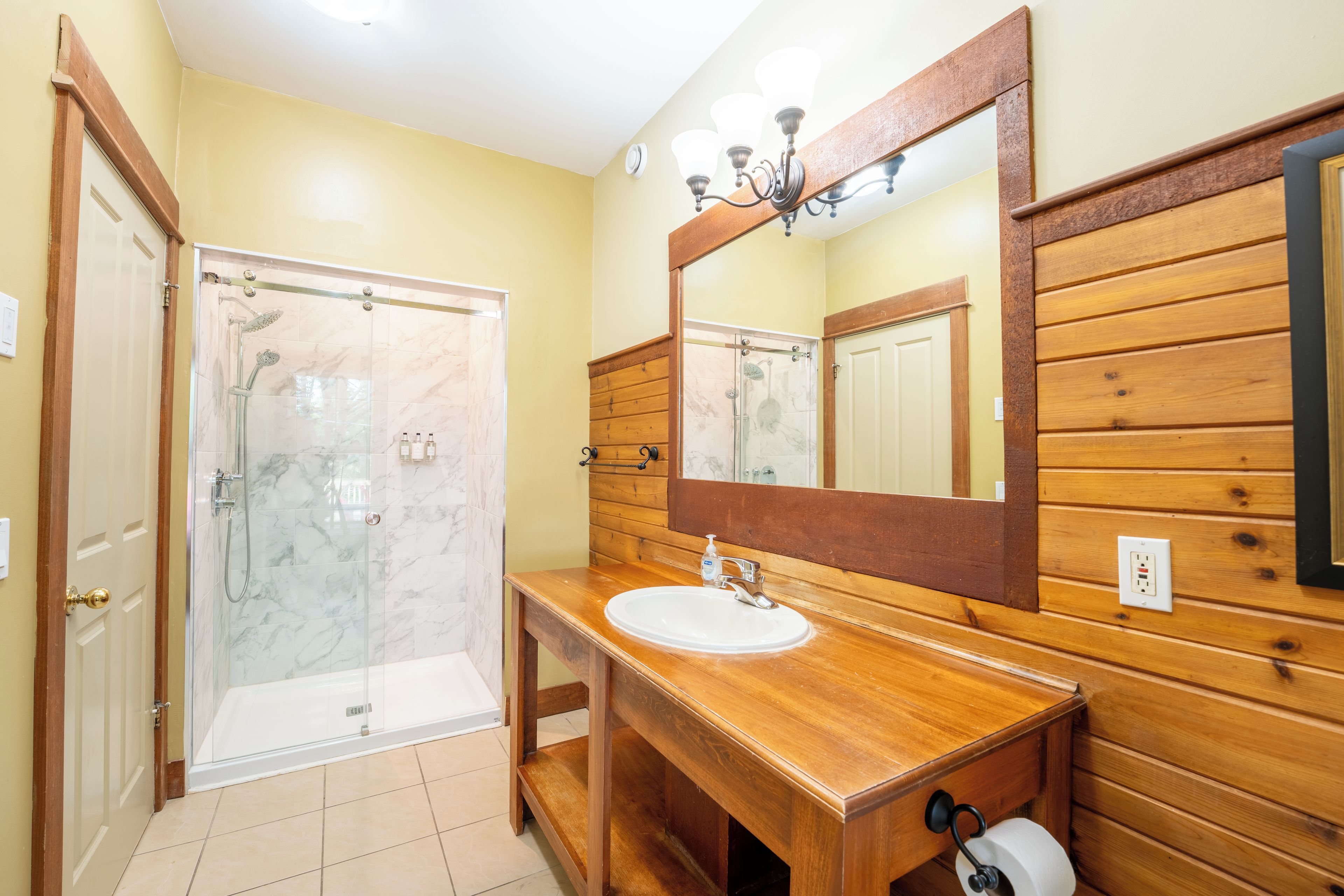 A bathroom with a glass shower enclosure, a wooden vanity with a sink, and a large mirror.
