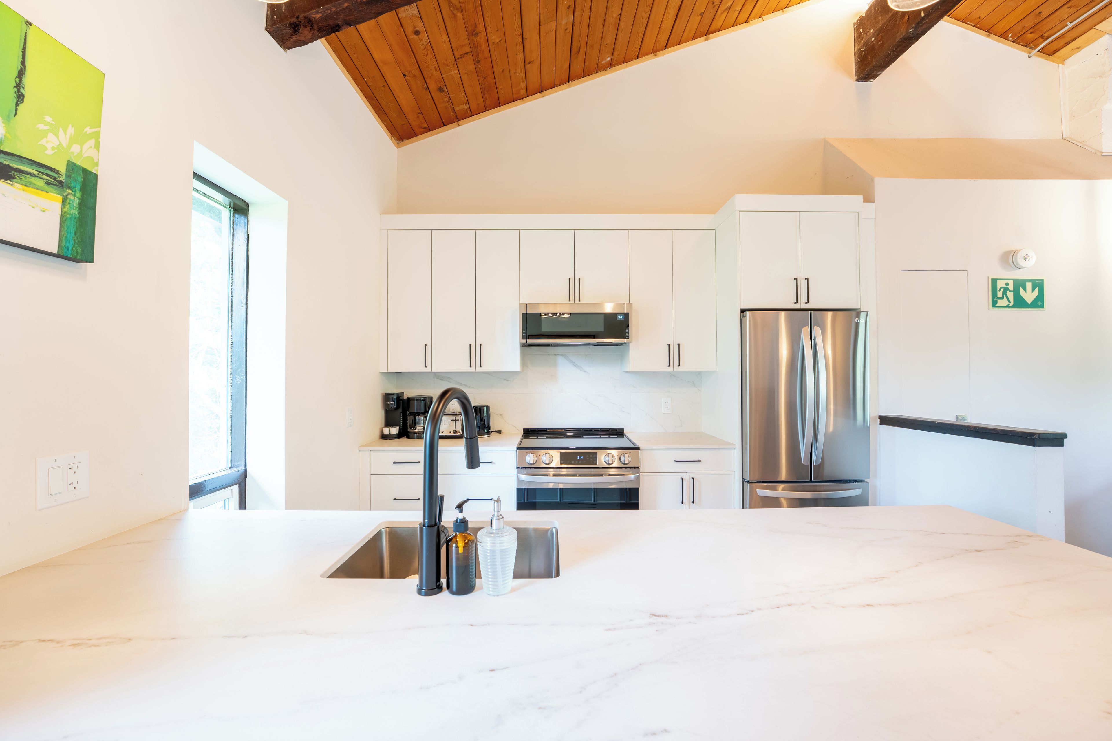 A modern kitchen with white cabinets, stainless steel appliances, and a marble countertop.