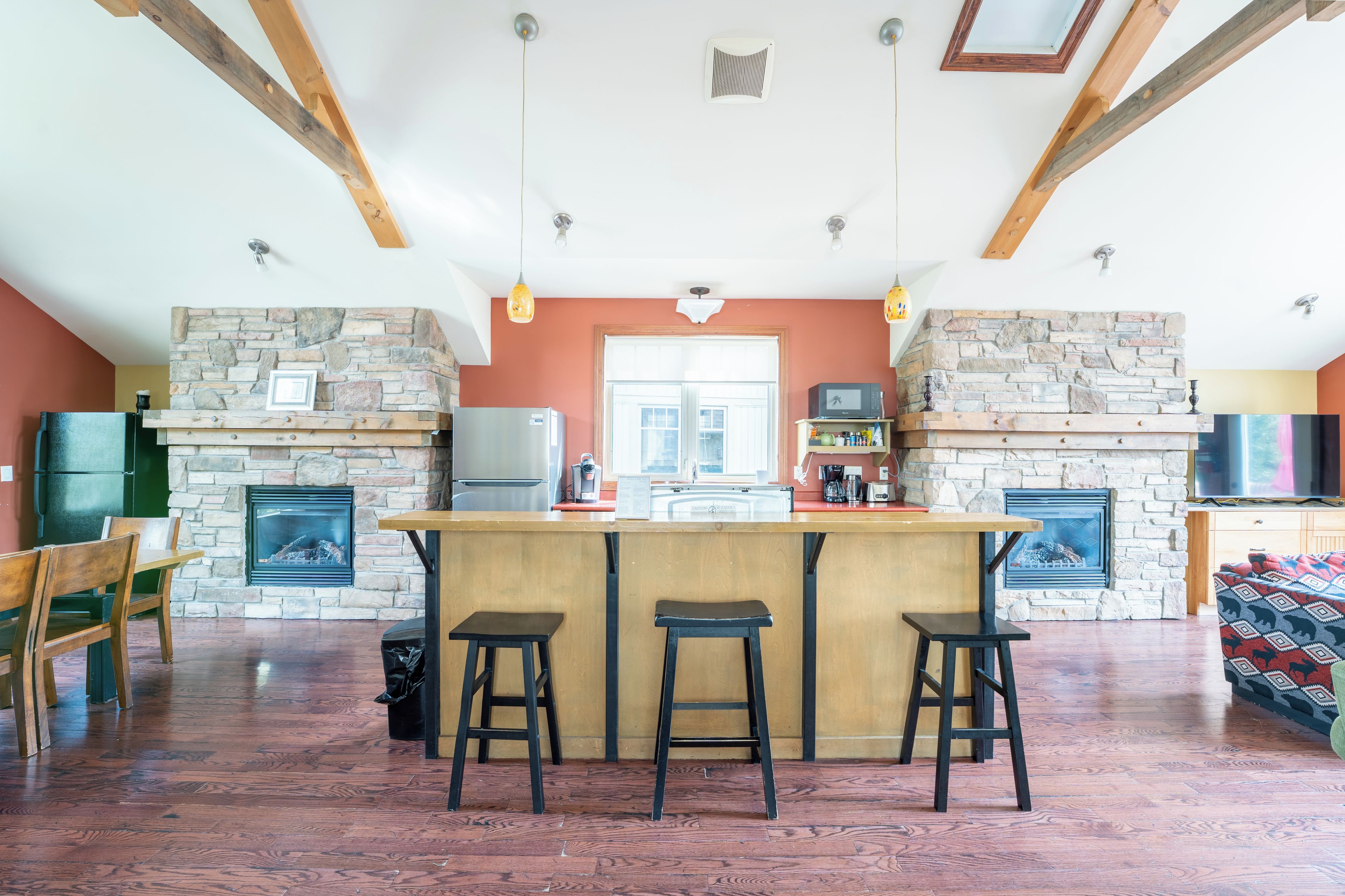 A spacious living area with a stone fireplace, wooden beams, and a bar with stools.