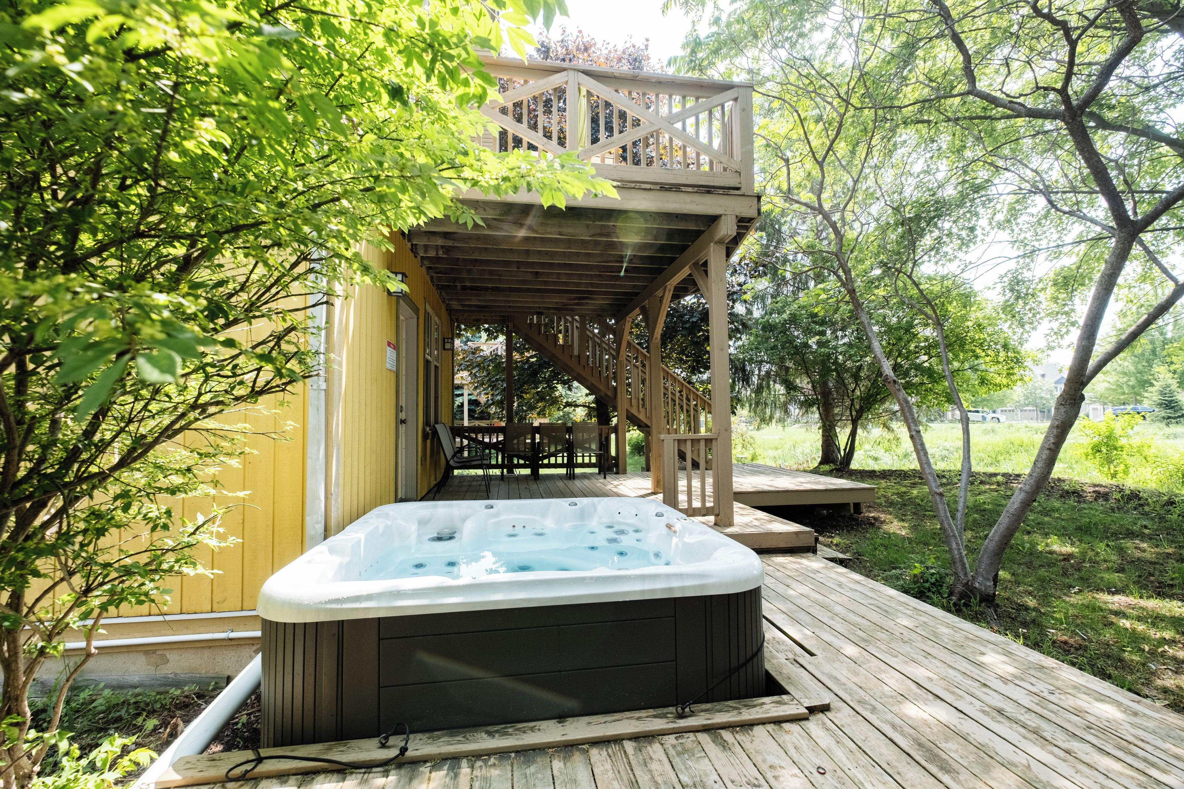 A hot tub on a wooden deck with a wooden staircase leading to a decked area.