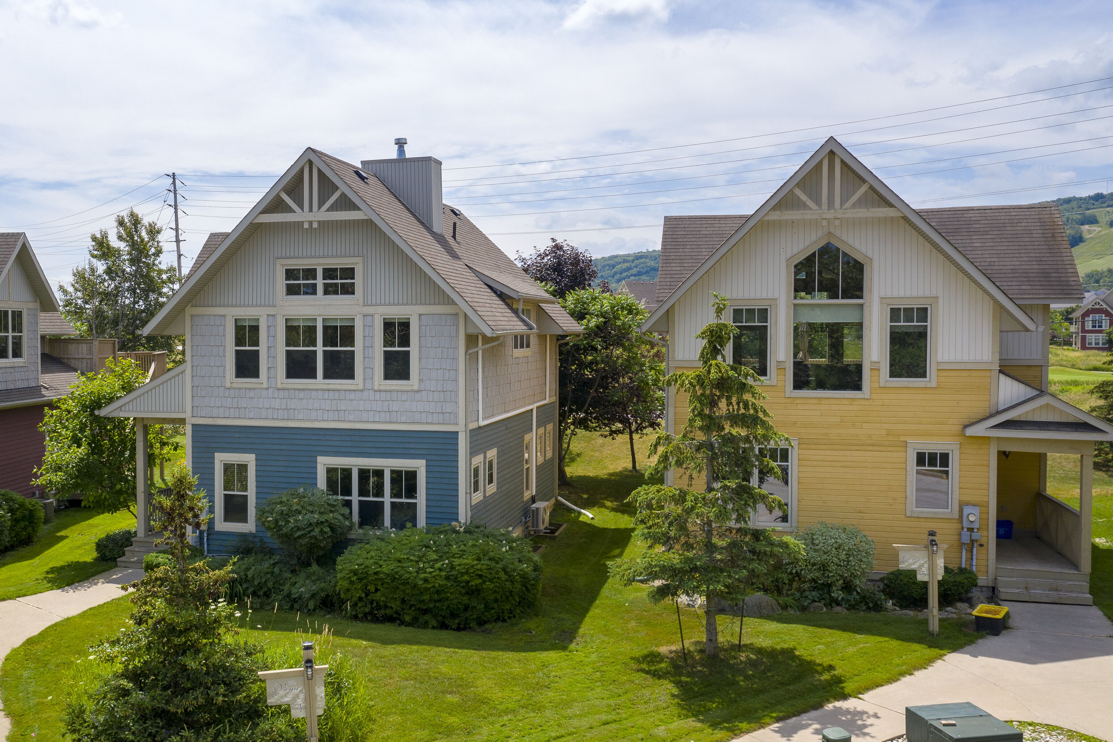 A row of two-story houses with pitched roofs, surrounded by well-maintained lawns and trees.