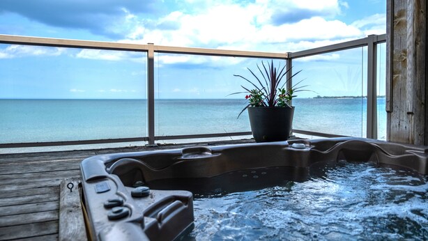 A hot tub with a view of the ocean, a wooden deck, and a potted plant. - Blue View Chalets (The Blue Mountains)