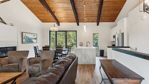 A modern living room with a leather sofa, wooden dining table, and a kitchen area with white cabinets and a stainless steel refrigerator. - Blue View Chalets (The Blue Mountains)