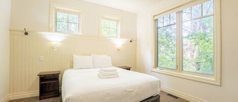 Un dormitorio con una cama grande, dos mesitas de noche, una lámpara de noche, una ventana con vistas a árboles y luces fijadas en la pared.