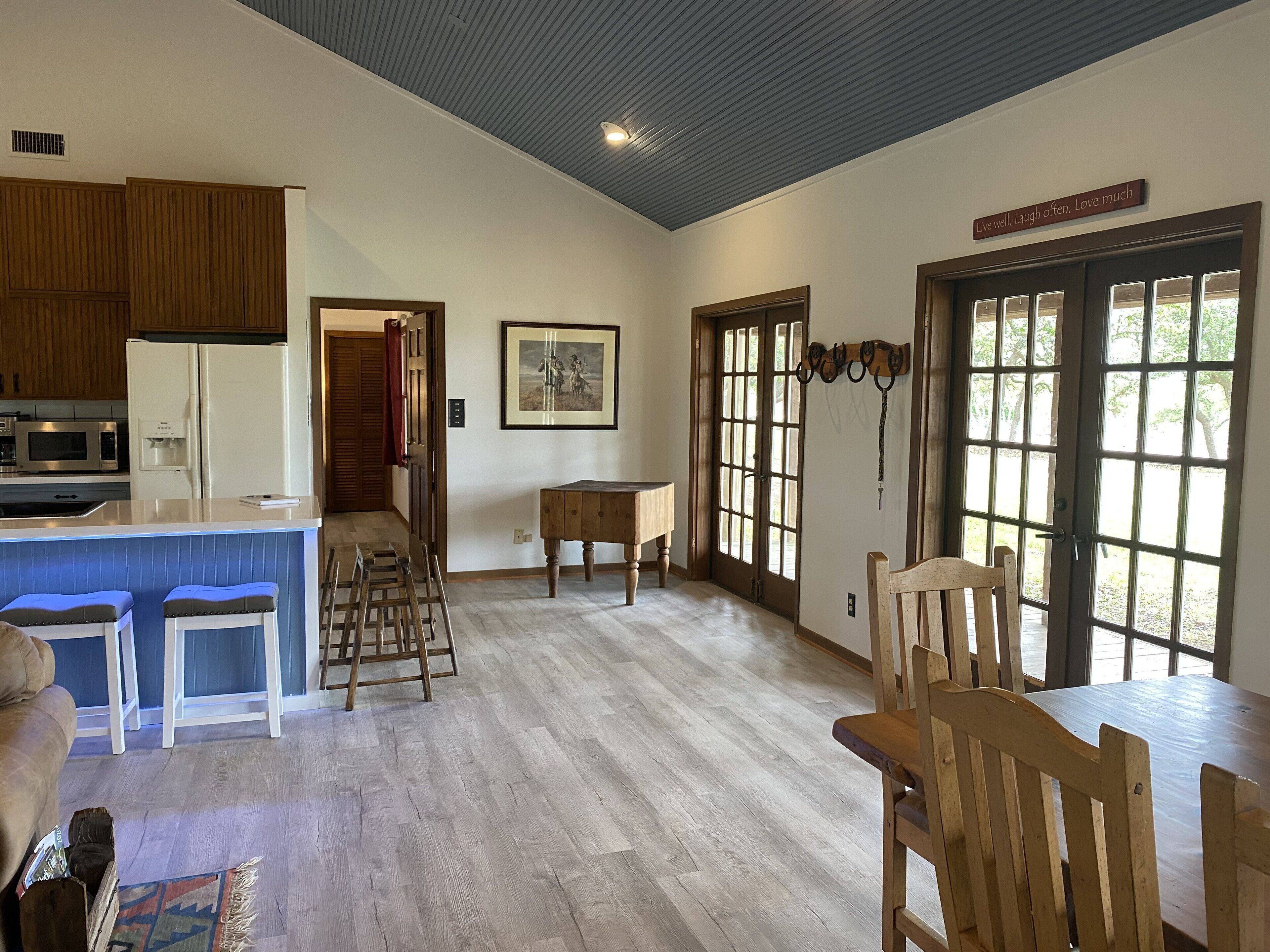 Cocina amplia con armarios de madera, microondas y refrigerador. Hay un comedor con mesa y sillas de madera, y una barra con taburetes.