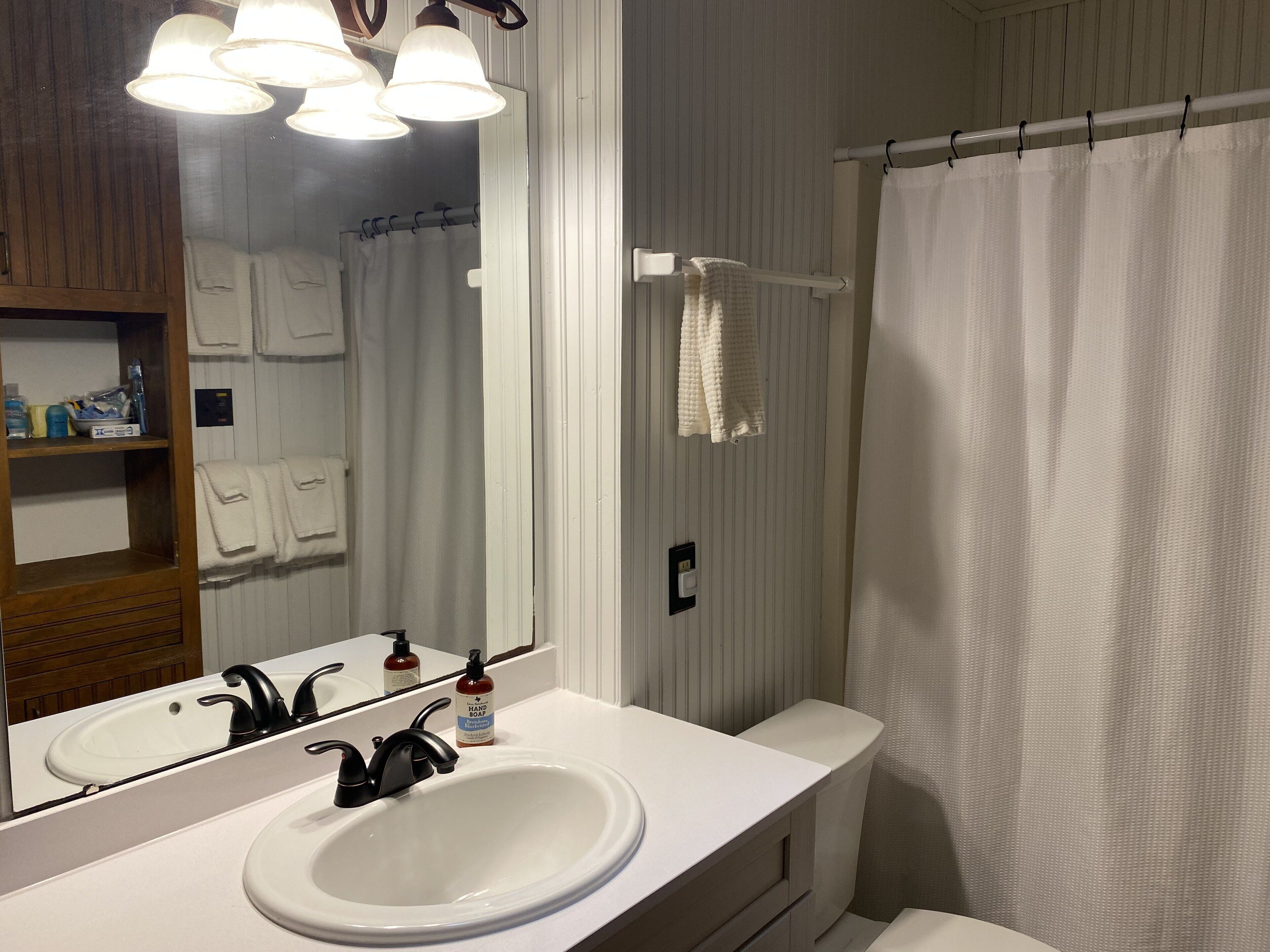 A bathroom with a white sink, black faucet, and a mirror above it. There are towels hanging on a rack and a shower curtain.