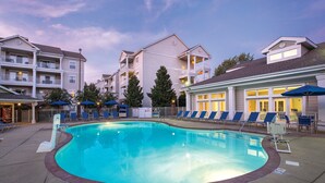 A swimming pool with lounge chairs and umbrellas, surrounded by multi-story buildings with balconies.
