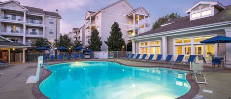 A swimming pool with lounge chairs and umbrellas, surrounded by multi-story buildings with balconies.