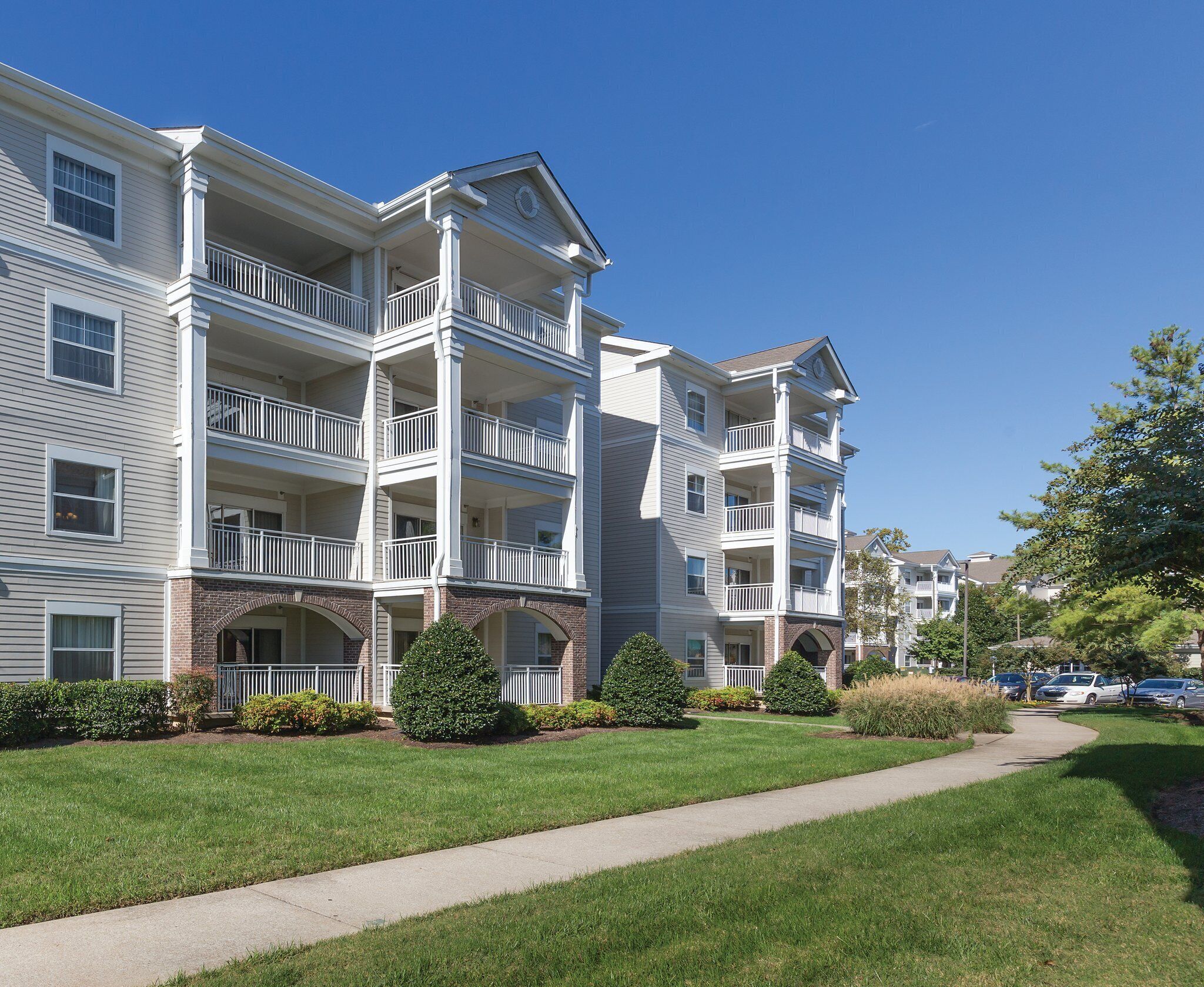 A multi-story apartment building with balconies, brick archways, and a well-maintained lawn.