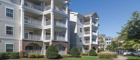 A multi-story apartment building with balconies, brick archways, and a well-maintained lawn.