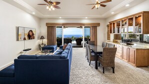 A spacious living room with a blue sofa, dining area, kitchen, and a view of the ocean.