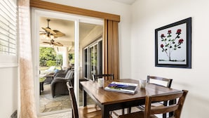A dining area with a wooden table, chairs, and a magazine. There is a sliding glass door leading to an outdoor patio with furniture.