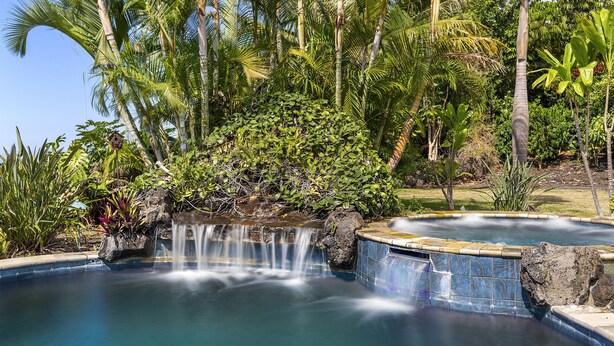 A pool with a waterfall feature surrounded by tropical vegetation.