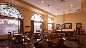 A hotel lobby with a large sofa, multiple chairs, a dining table, and a TV.