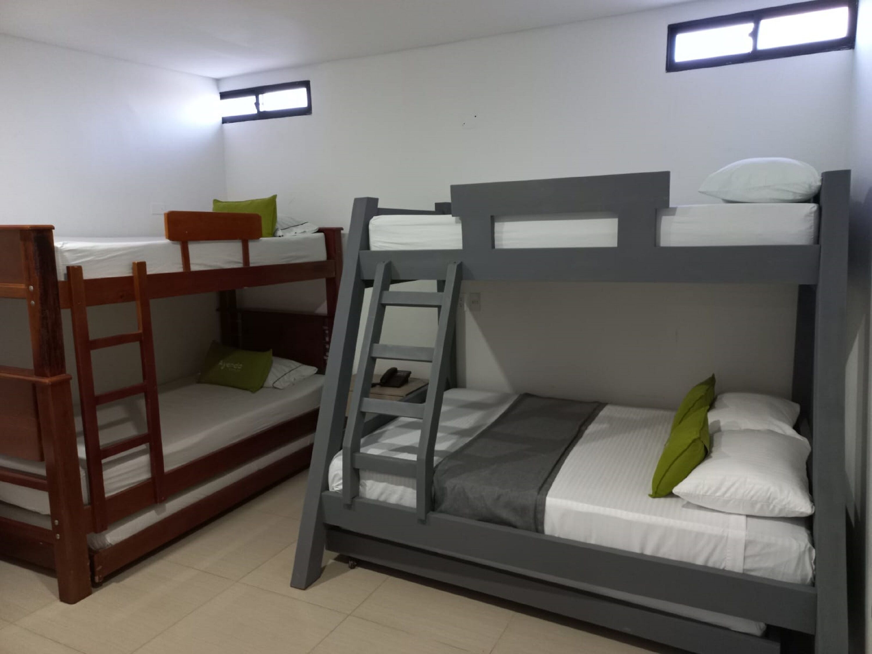 A dormitory room with two bunk beds, a ladder, and a small window.