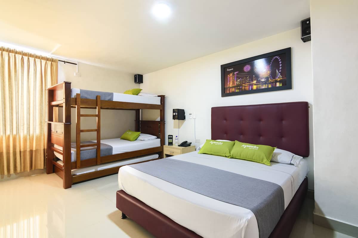 Een hotelkamer met een groot bed, een kleiner stapelbed, een nachtkastje, een lamp en een foto van een stadsgezicht aan de muur.