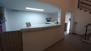 Un comptoir d’accueil avec une pancarte, une plante en pot et un escalier en arrière-plan.