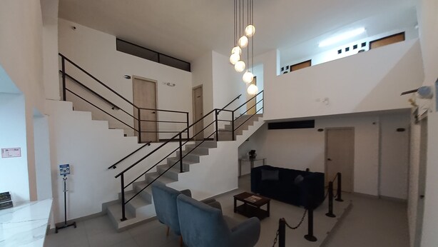Un vaste espace de vie comprenant un escalier, un fauteuil bleu, une table basse et un canapé noir.