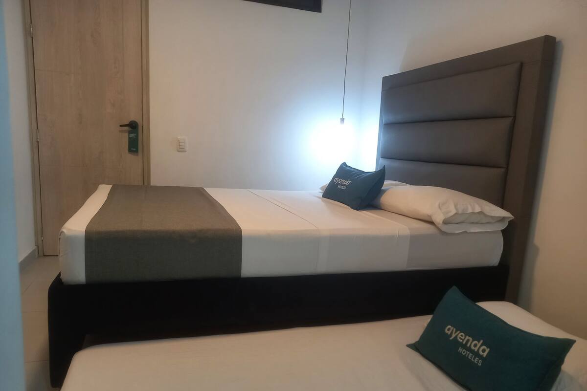 Een hotelkamer met een bed, nachtkastje, wandlamp en een deur.