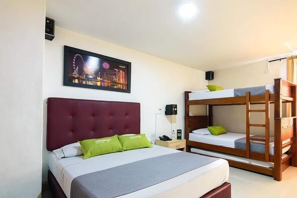 Een hotelkamer met een enkel bed, een stapelbed, een nachtkastje, een lamp en een ingelijst foto aan de muur.