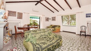 Um quarto acolhedor com um sofá estampado, uma mesa de jantar e cadeiras. Há quadros nas paredes e uma janela com vista para o verde.