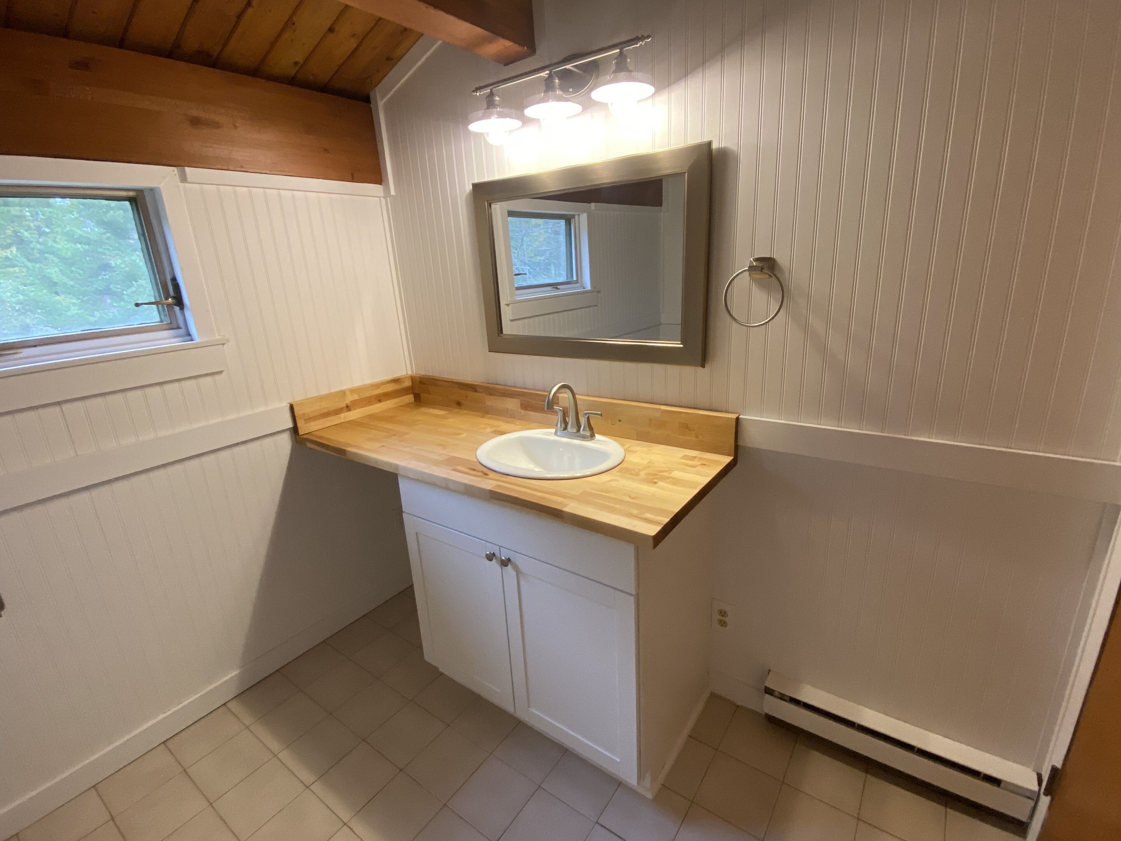 Ein Badezimmer mit einem Holzbadschränke, weißen Schränken, einem Waschbecken, einem Spiegel und einem Fenster.