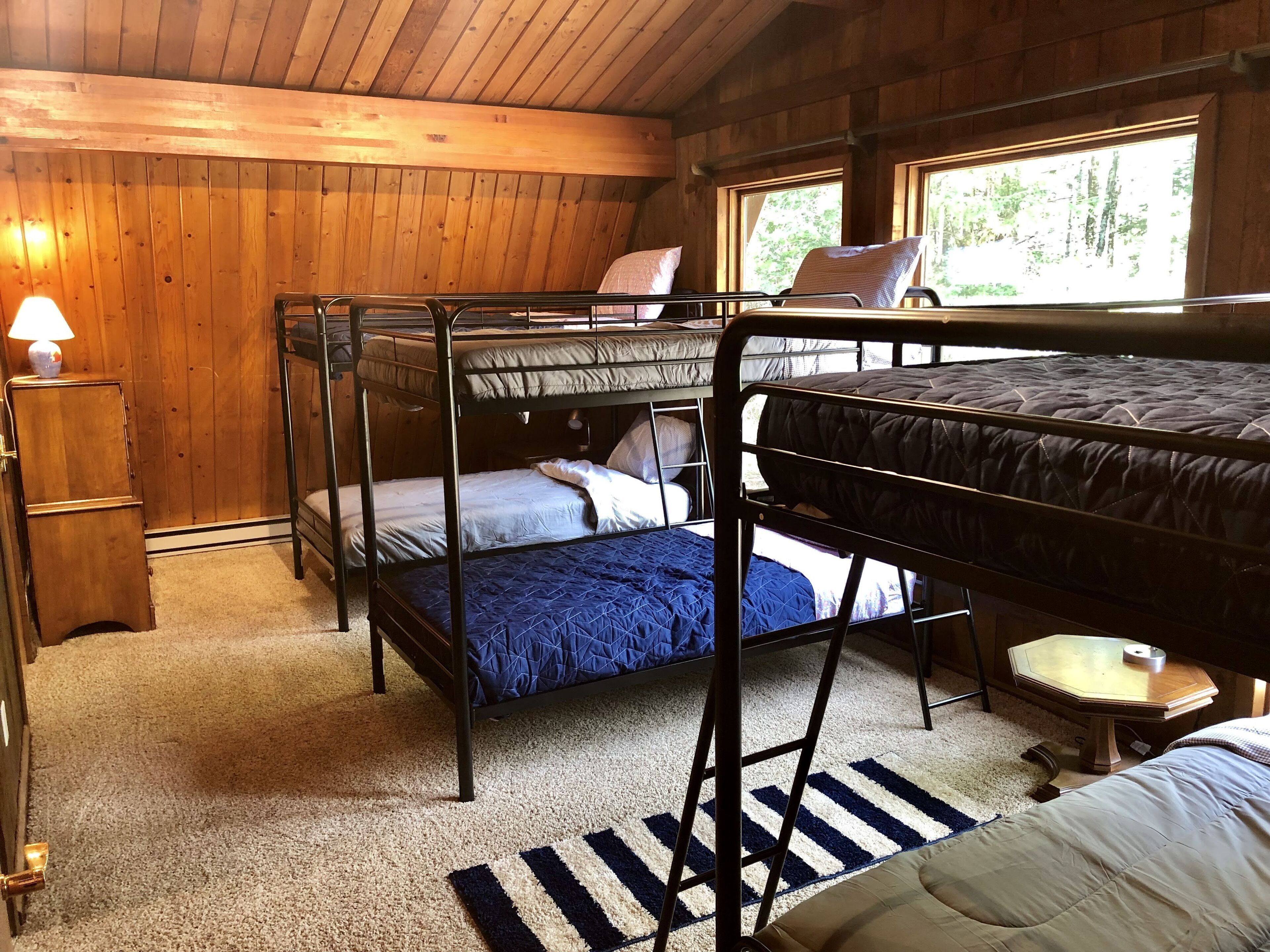 Une cabine avec des lits superposés, une armoire en bois, une lampe et une fenêtre donnant sur les arbres.