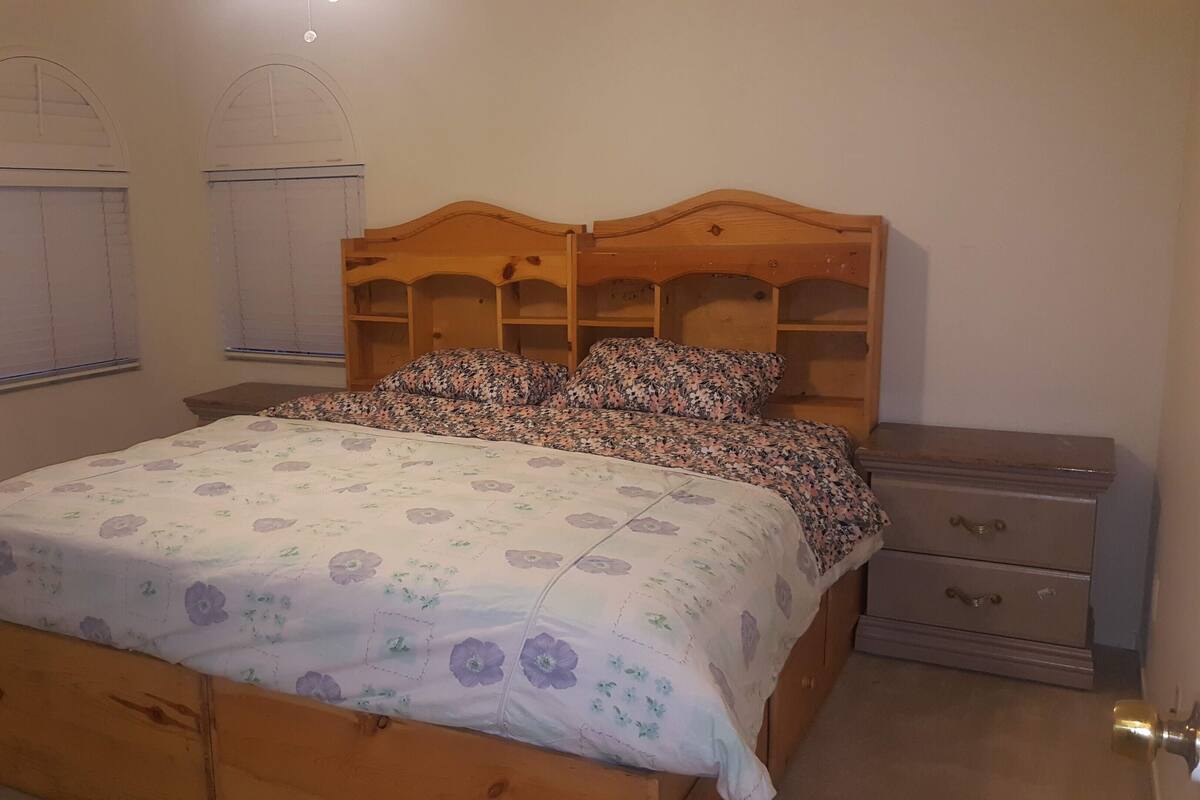 A bedroom with a wooden bed, floral bedding, a nightstand, a dresser, and two windows with shutters.