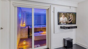 A room with a sliding door leading to a cozy seating area with a heater, a television mounted on the wall, and a small black speaker. - Greenhill Pension (Pyeongchang)