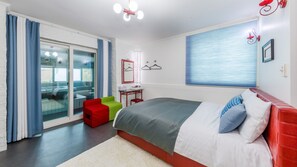 A modern bedroom with a bed, a red and green chair, a small table, and a large window with blinds. - Greenhill Pension (Pyeongchang)