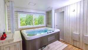 A bathroom with a wooden interior, a window with a view of greenery, a bathtub, and a small table with glasses and a bottle. - Greenhill Pension (Pyeongchang)