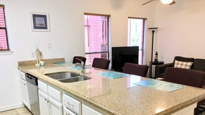 A kitchen with a granite countertop, stainless steel sink, and white cabinetry. There are two windows with blinds, a small framed picture on the wall, and a floor lamp. - Simple & Comfortable just like Home - mins walk to Beach - Max 2 Adults + 2 Kids (South Padre Island)