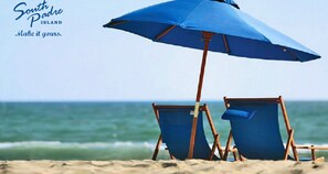 A beach scene with two blue beach chairs and a blue umbrella.