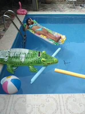 A swimming pool with a person lying on a float, a large inflatable crocodile, and a beach ball. - Yucatan Vista Inn (Mérida)