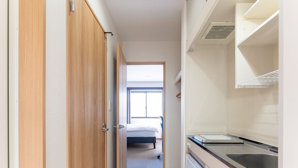 Un pasillo estrecho que conduce a un dormitorio con ventana, una kitchenette con lavabo y un baño pequeño.