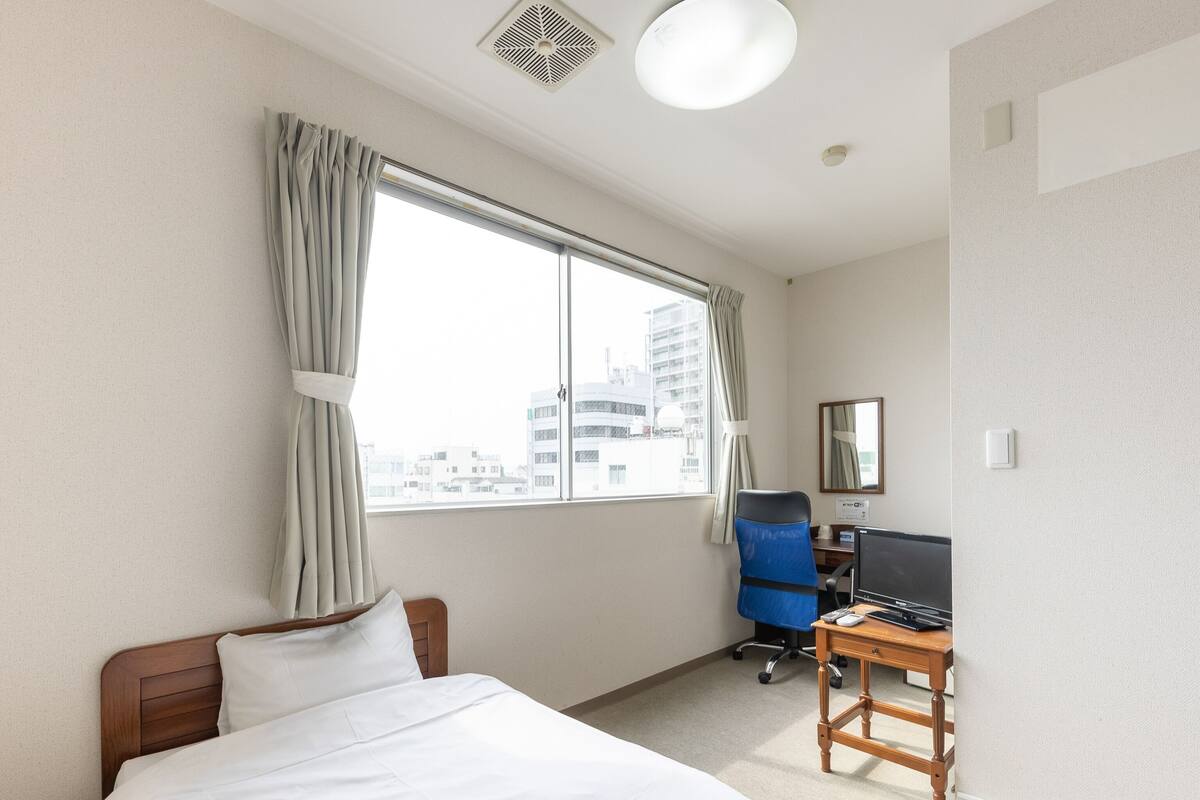 Una habitación de hotel con cama, escritorio con computadora, silla y ventana con cortinas.