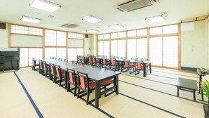 Un salón de conferencias con una larga mesa y sillas, ventanas amplias y luces en el techo.