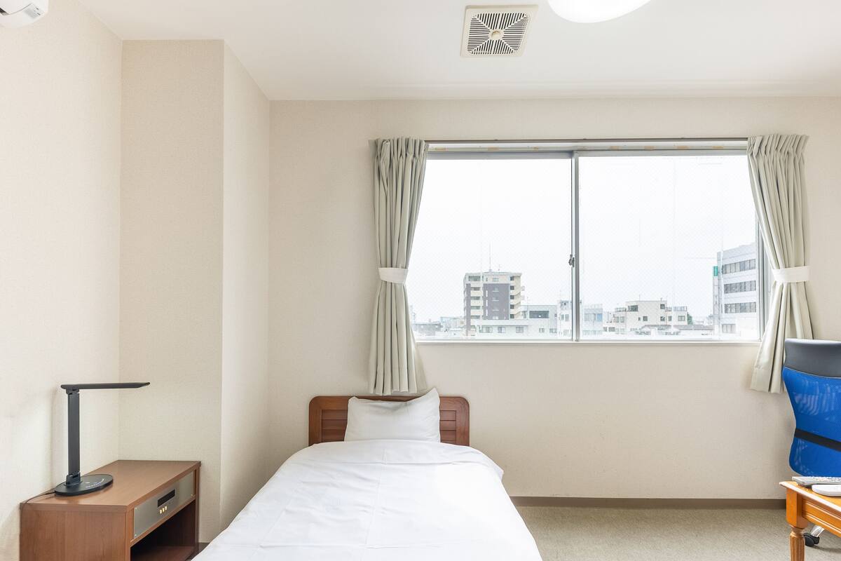 Una habitación de hotel con cama, escritorio, silla y ventana con cortinas.