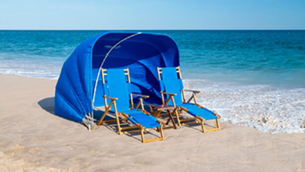 Une plage avec une tente bleue et des chaises longues en bois.