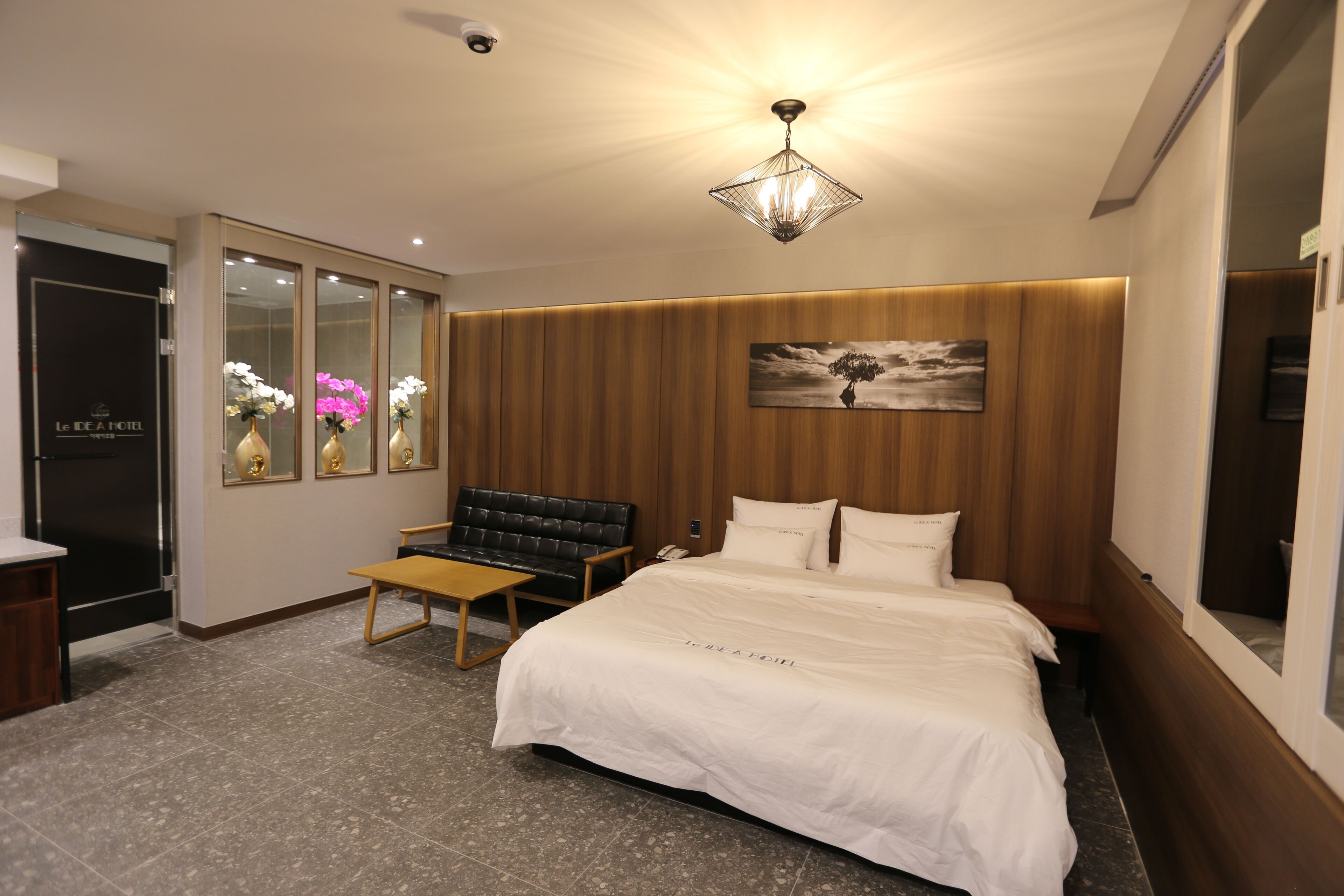 A hotel room with a large bed, a wooden headboard, a bench, a small table, and a wall-mounted painting.