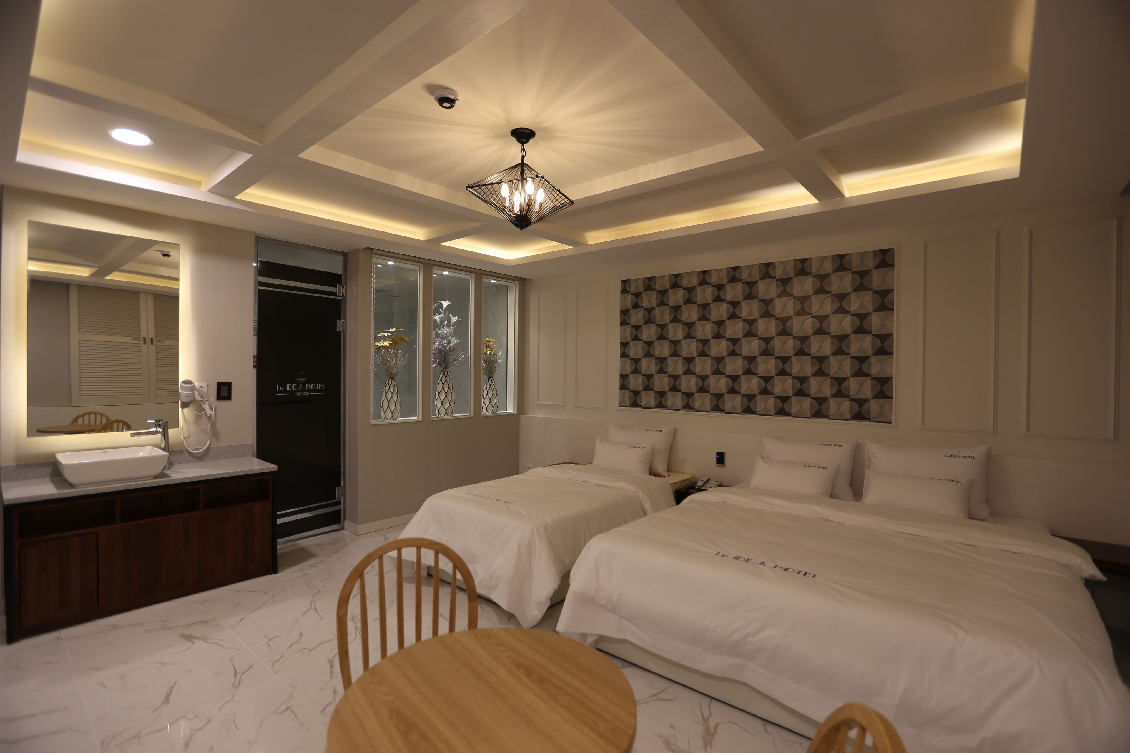 Quarto de hotel com duas camas, banheiro com pia e área de refeições com mesa e cadeiras.