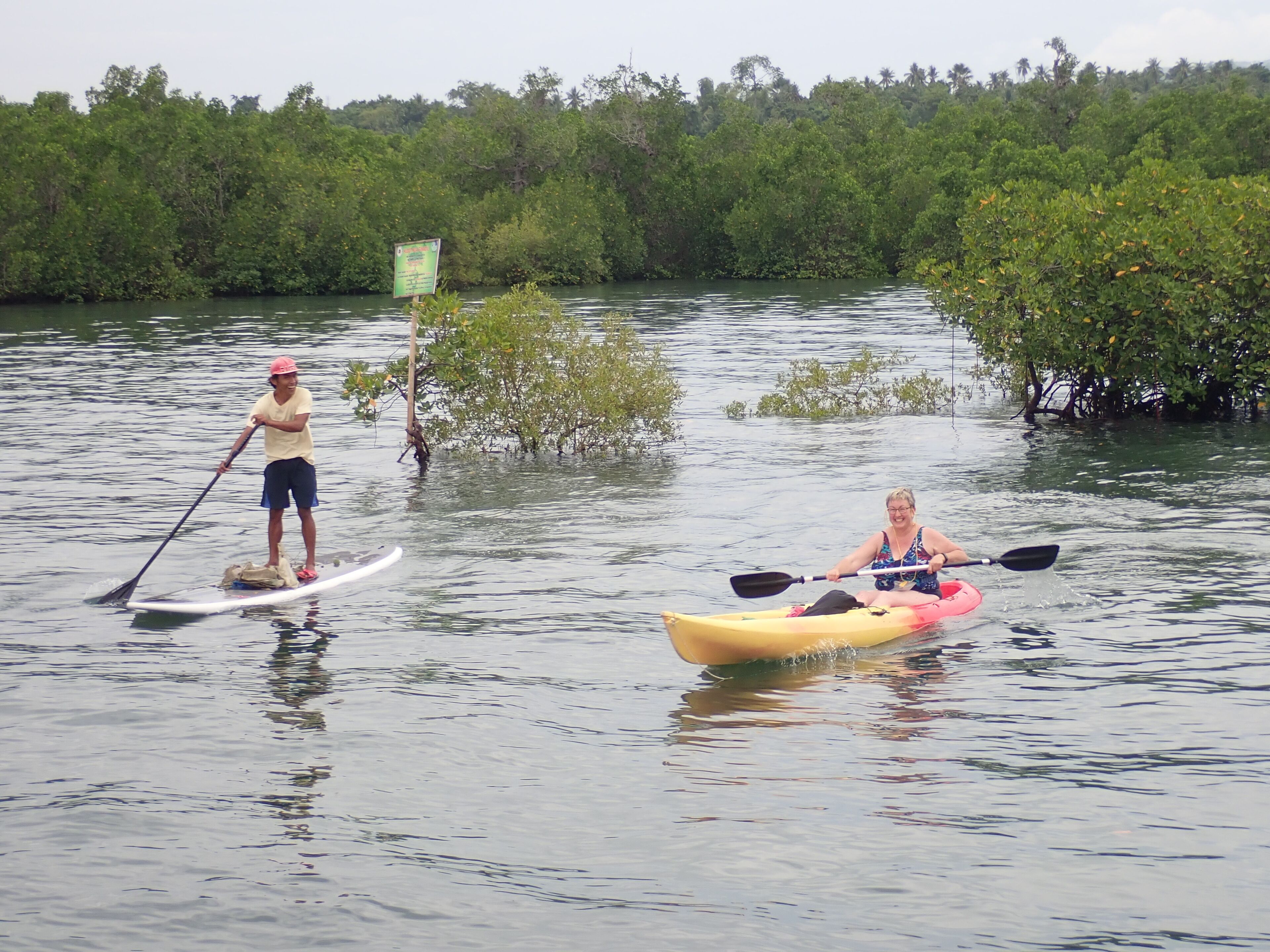 Dos personas hacen kayak en un río tranquilo rodeado de densos manglares.
