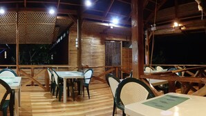 A restaurant with wooden tables and chairs, a covered seating area, and large windows. - Eskapo Verde Lodge Moalboal (Badian)